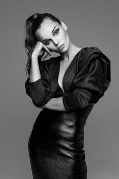 a woman posing for a black and white photo wearing a leather skirt with her hands on her head