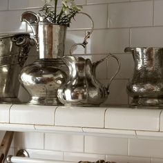 some silver pots are sitting on a white shelf with flowers in the vase and other metal containers