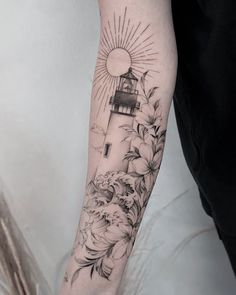 a person with a tattoo on their arm that has flowers and a lighthouse in the background