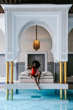 a woman in an orange dress is sitting on a white bench near a swimming pool