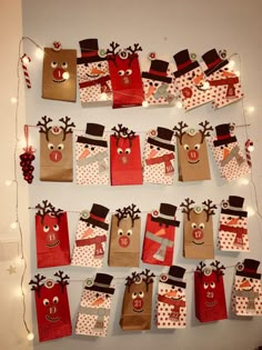 paper bags with reindeer faces and hats on them are hanging from a wall decorated with christmas lights