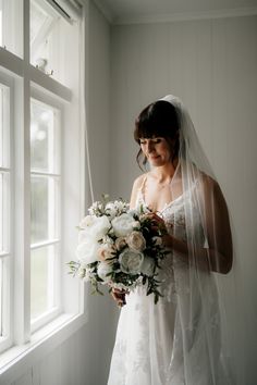 a woman standing in front of a window holding a bouquet