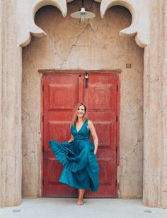 a woman standing in front of a red door wearing a teal dress and heels