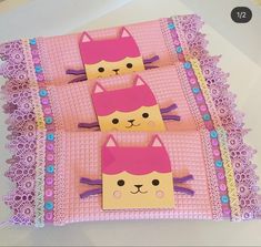 three paper cats are sitting on top of pink doily with purple lace around them