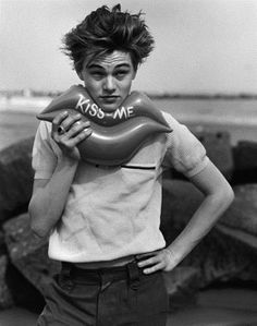 black and white photograph of a young man holding an inflatable object with the word kiss me on it