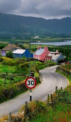 a street sign sitting on the side of a road near a lush green field and mountains