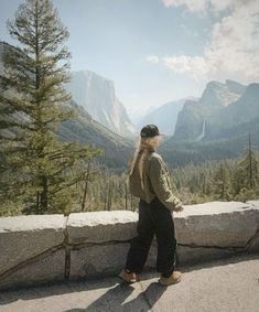 a woman standing on the edge of a cliff looking at mountains and trees in the distance