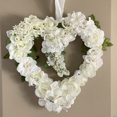 a heart shaped wreath with white flowers hanging on the wall