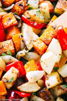 a wooden spoon is in a bowl full of roasted veggies and potatoes with herbs