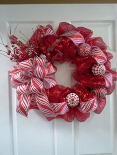 a red and white wreath on a door with candy canes hanging from it's side