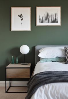 a bedroom with green walls and two pictures on the wall above the bed, along with an end table