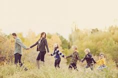 a group of children holding hands and walking through tall grass with their mother in the background