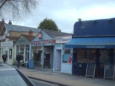 an old fashioned store on the corner of a street with people walking by and cars parked in front