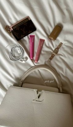 the contents of a handbag are laid out on a white bed with a purse