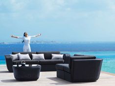 a woman standing on top of a black couch near the ocean