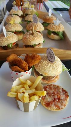 sandwiches and french fries are sitting on a table with trays of other food in the background