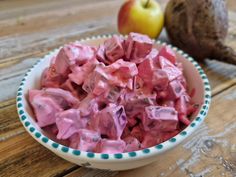 a bowl filled with pink jello next to an apple on top of a wooden table