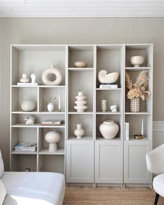 a living room filled with lots of white vases on top of bookshelves