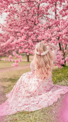 a woman with long pink hair sitting on the ground in front of some cherry trees