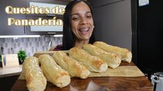 a woman smiles as she holds up some breads on a cutting board with the words quesitos de panaderia in front of her