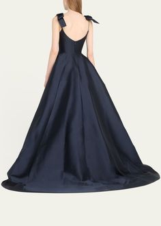 the back of a woman wearing a dark blue gown with an open neck and bow at the