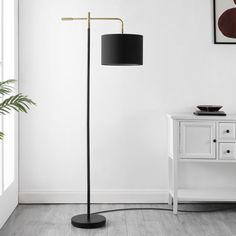 a black floor lamp next to a white cabinet and potted plant on a table