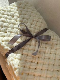 two white crocheted blankets with a brown ribbon tied around the edges, stacked on top of each other