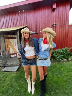 two women in cowboy hats standing next to each other on the grass near a barn