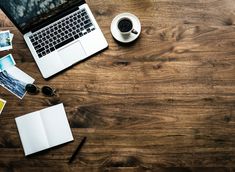 an open laptop computer sitting on top of a wooden desk next to a cup of coffee