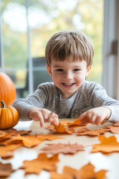 Smiling child playing with autumn leaves indoors near pumpkins.