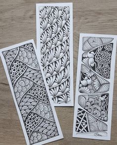 three cards with intricate designs on them sitting on top of a wooden table next to each other