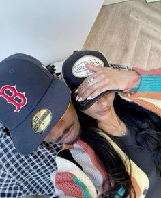 a man and woman laying on top of each other wearing baseball caps with their faces close together