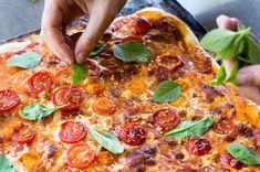 a pizza with tomatoes and basil on it being held up by someone's hand