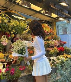 a woman is looking at flowers in a flower shop while wearing a short white dress