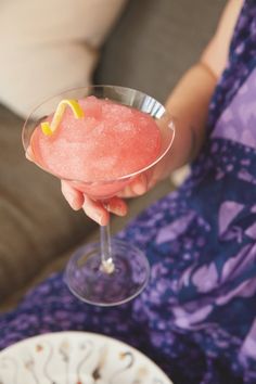 a woman holding a wine glass filled with pink liquid and topped with a lemon wedge