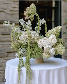 two vases filled with white and green flowers on top of a round tablecloth