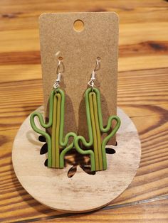 a pair of green cactus earrings sitting on top of a wooden stand next to a card