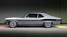 an old muscle car is parked in front of a garage door with its lights on