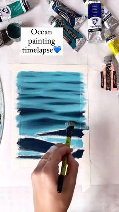 someone is painting the ocean with blue and green colors on paper, while other paints are scattered around