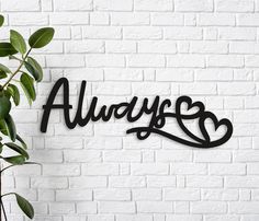 the word always with hearts is mounted on a white brick wall next to a potted plant