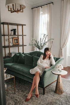 a woman sitting on top of a green couch in a living room next to a window