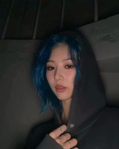 a woman with blue hair wearing a black hoodie and holding her hands on her chest