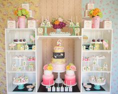 a table topped with lots of cakes and cupcakes on top of it's shelves