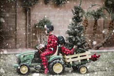 a man riding on the back of a green tractor in snow covered yard next to a christmas tree