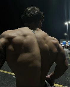 the back of a man with no shirt on walking down a street at night time