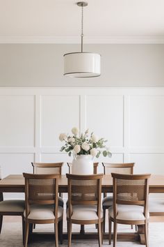 a dining room table and chairs with flowers in a vase on the top one side