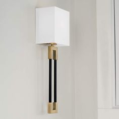 a white square light hanging from the side of a wall next to a black and gold lamp