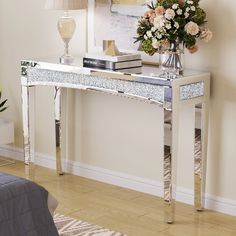 a white and silver console table with flowers in vase next to lamp on hard wood floor