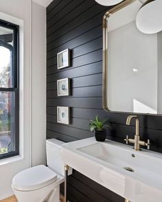 a white toilet sitting under a bathroom mirror next to a sink with a potted plant on top of it