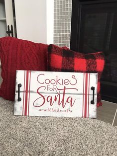 a wooden sign that says cookies for santa on it next to some red and white pillows